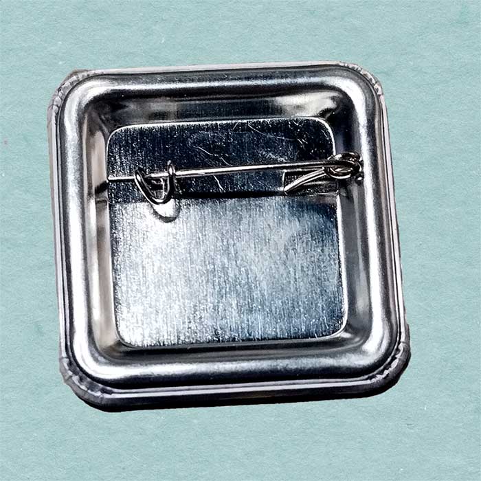 Metallic square brooch with a clasp on a light blue background