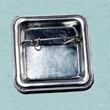 Metallic square brooch with a clasp on a light blue background
